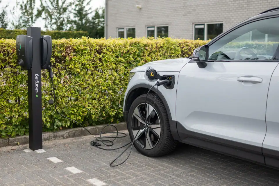 Een E-Charging-laadpaal bij de haag laadt een witte elektrische auto
